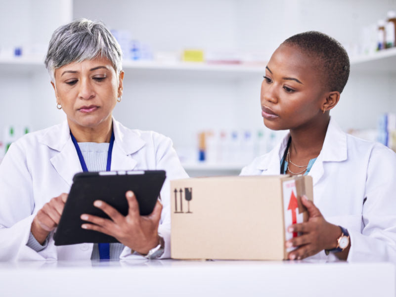 Two women in lab coats looking at a tablet.